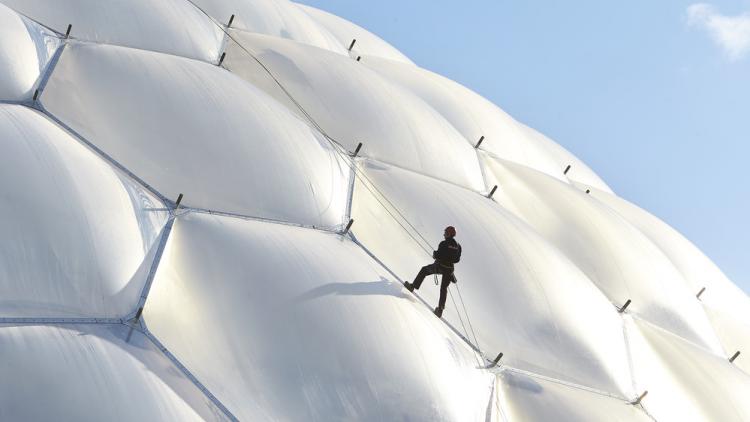 Individual scaling the Biome in a climbing harness