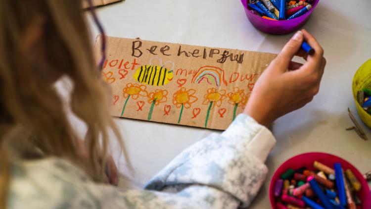 Girl making a save the bees placard with crayons