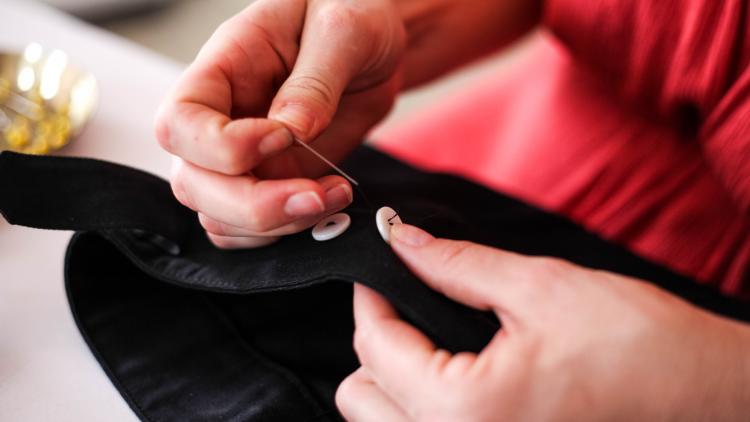 Hands sewing button onto garment