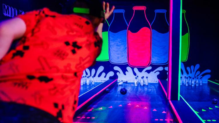 Boy throwing bowling ball towards skittles in neon room