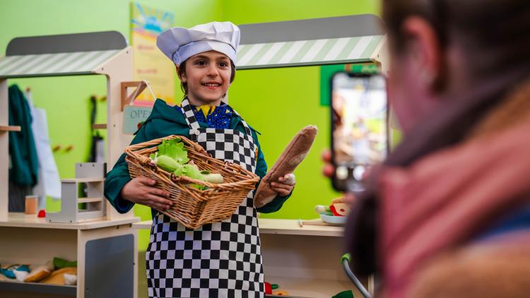 Boy in chef costume holding baguette and basket with pretend food inside