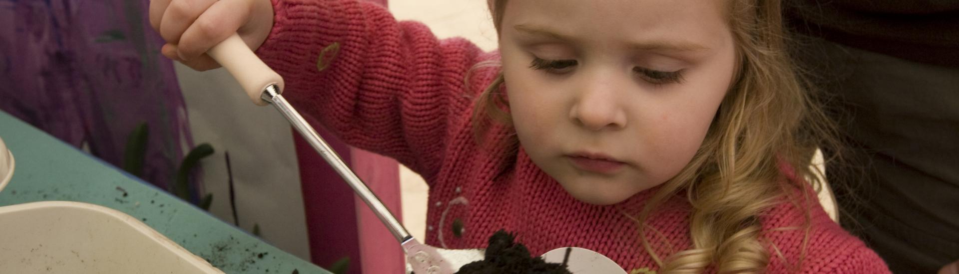 A young girl putting a spoon of soil into a paper cup 
