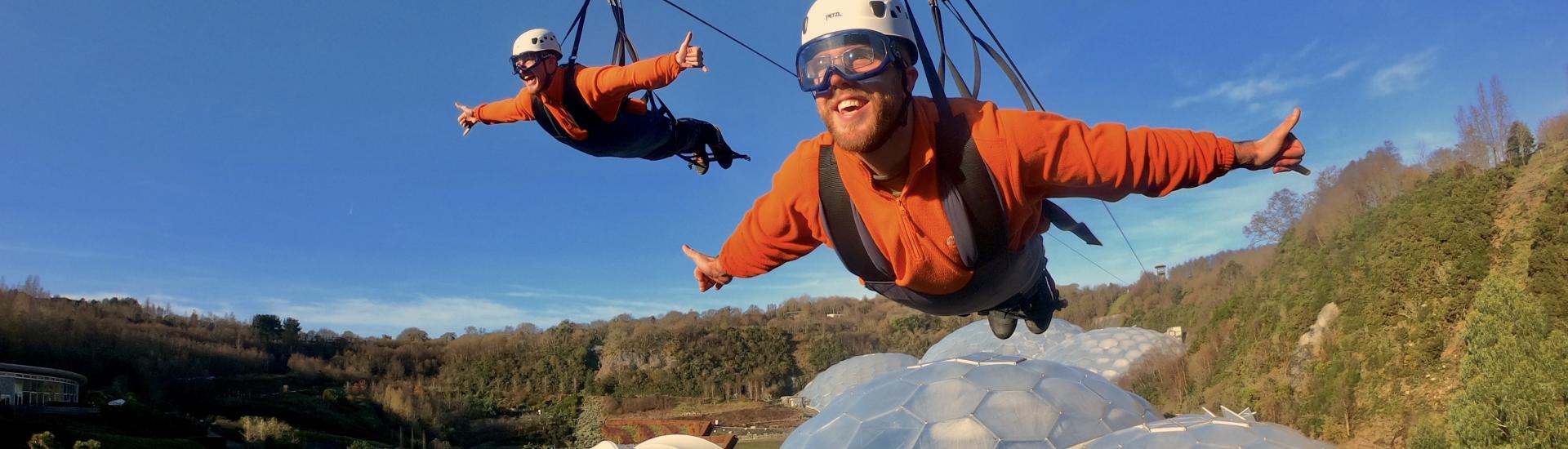 Two people going along the zip wire over the Eden biomes