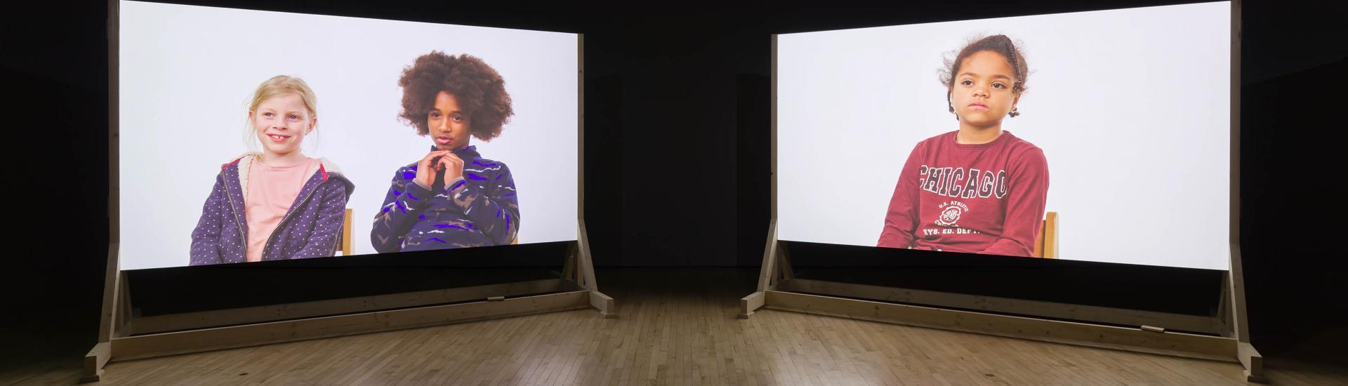 Two screens with films of children talking projected on them 