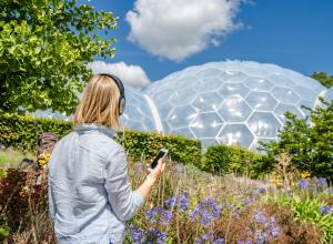 A picture of someone looking at the Eden biomes and holding their phone with their headphones on 