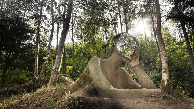 A view of a giant figure sculpture emerging from the ground with a mirrored mosaic face