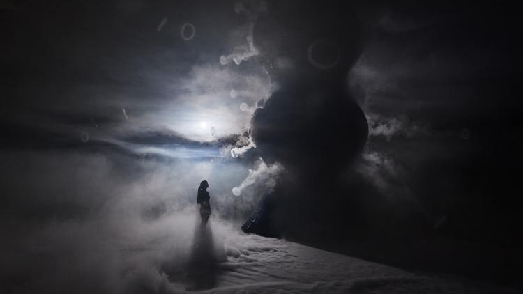 An atmospheric photo which shows a figure standing looking up at the infinity blue sculpture and the vapour surrounding the floor and sculpture 