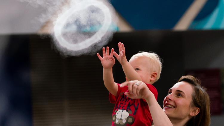 A young boy being held up by his guardian catching one of the rings coming out of infinity blue