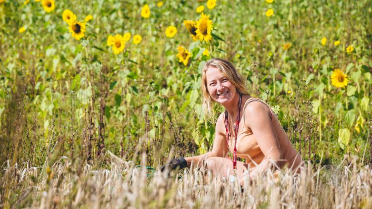 A Eden employee gardening looking to the camera surrounded by sunflowers