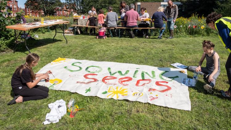 People in St Agnes Park, Liverpool, painting a big flag saying Sowing Seeds