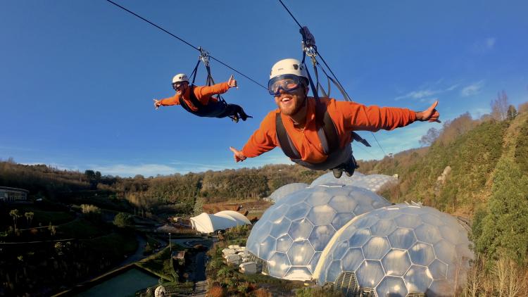 Two people going along the zip wire over the Eden biomes