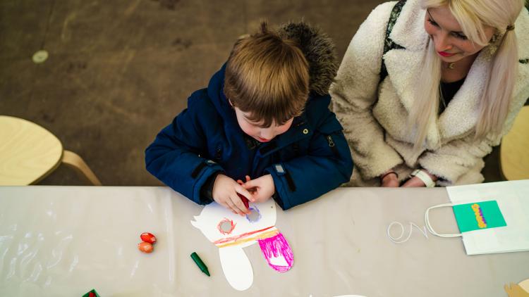 Child colouring in a rabbit mask with mum by his side