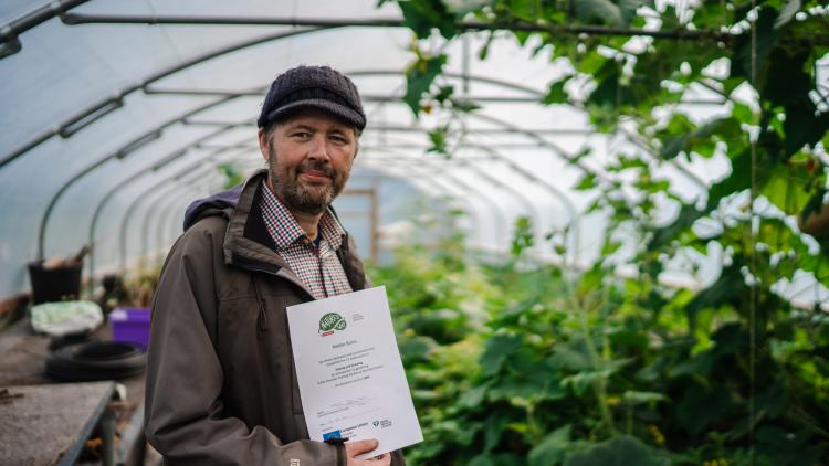 Man in polytunnel holding certificate