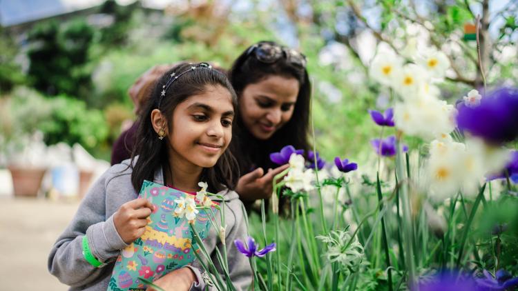Girl with Easter activity booklet and mother looking at spring flowers in Eden's Med Biome 