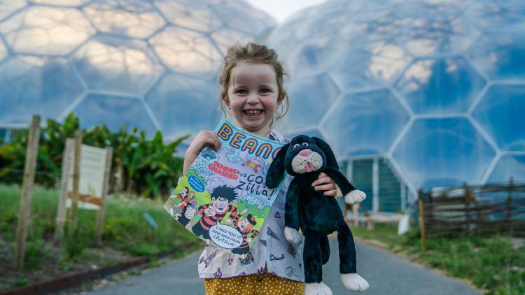 Girl holding Beano comic and toy dog in front of the Eden Project Biomes