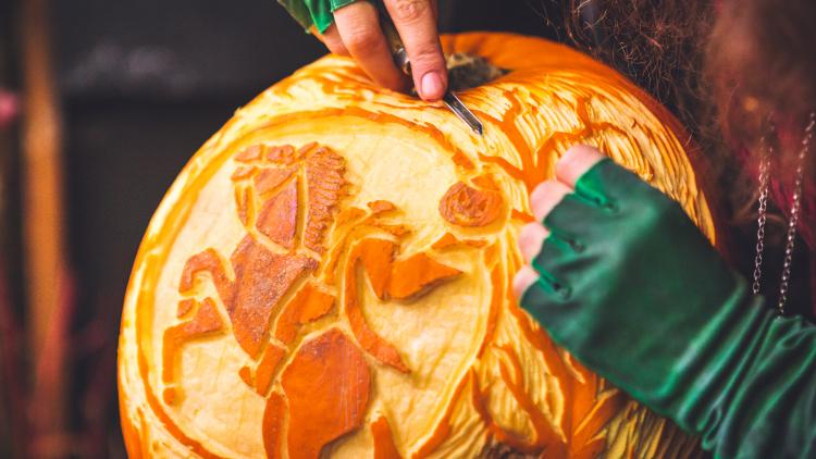 Hands carving a knight on a horse design into a pumpkin
