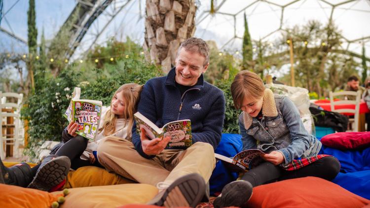 Family sat on cushions reading Tom Gates books in the Eden Project's Mediterranean Biome
