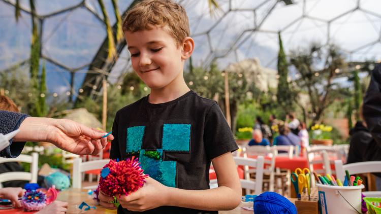 Boy holding a pom pom taking part in a craft activity in the Mediterranean Biome at the Eden Project