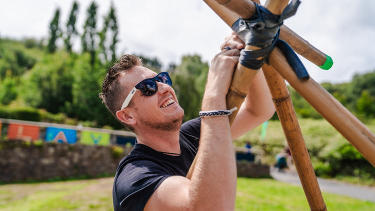 Man in black t-shirt and sunglasses smiling whilst making a den outside