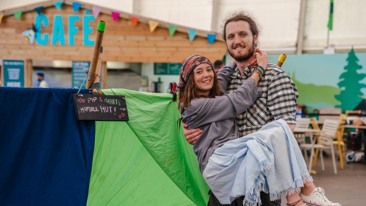 Man in a check shirt holding a woman in his arms standing in front of the den they created