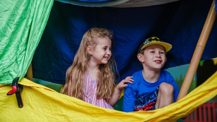 Young boy and girl smiling and hiding inside a den they created