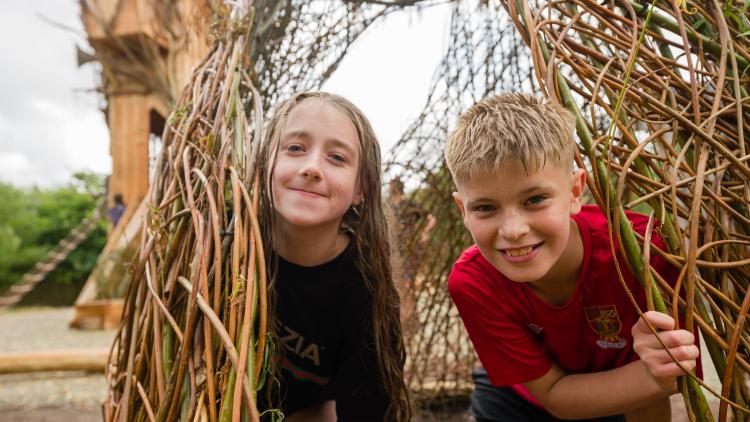 Boy and girl looking out of a willow den