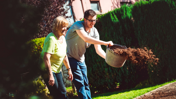 Man scattering soil from a bucket onto a garden