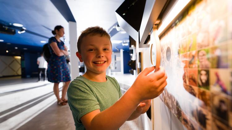 Boy in blue t shirt holding magnifying glass and smiling at camera