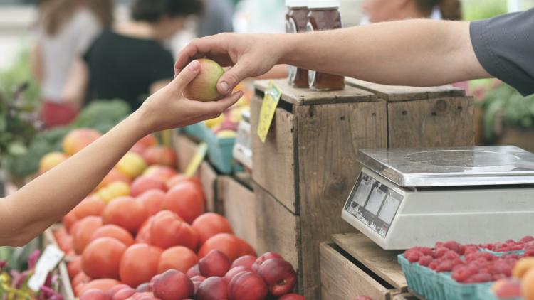 Hand passing apple to stall owner in a local market