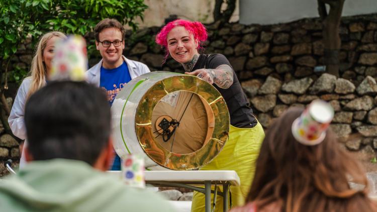 Lady holding large drum firing air to knock over paper cups