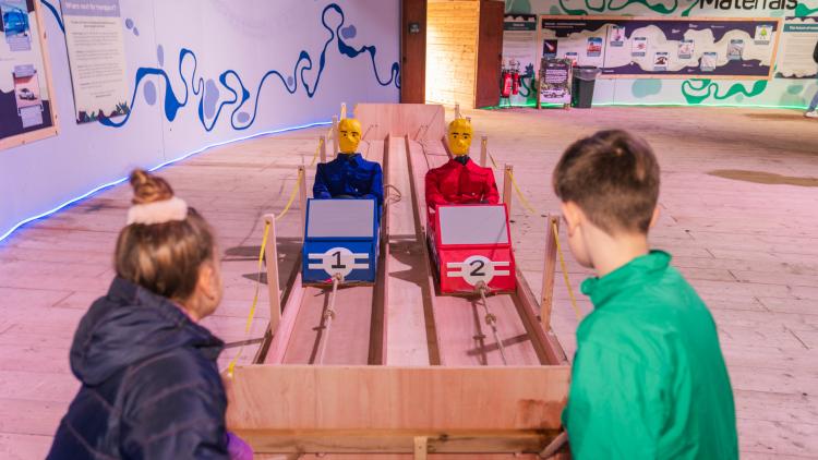 Two children pulling rope connected to large toy cars