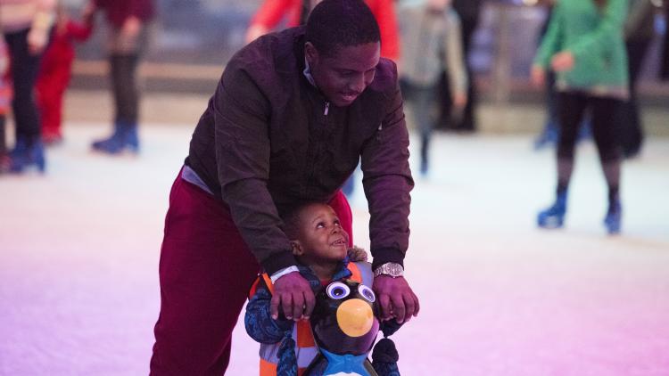 Father helping young son ice skate with penguin aid