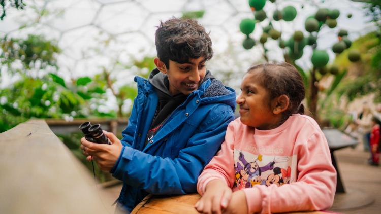 Boy and girl looking at each other holding binoculars in the Eden Project Rainforest