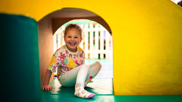 Girl hiding in archway under a slide in soft play