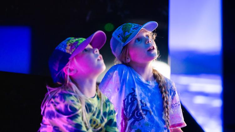 Girls looking up in a dark space filled with projections