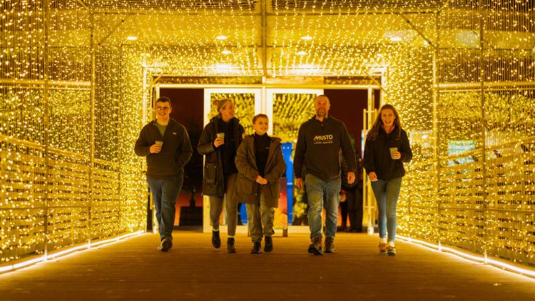 Family of five walking through the tunnel of lights link bride holding coffees and laughing