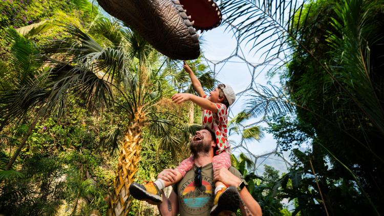 Child on father's shoulders reaching for a T-Rex