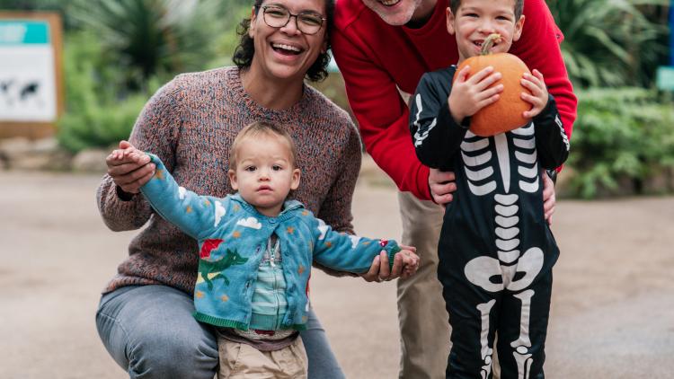 Family photo with child dressed up in skeleton costume holding a pumpkin