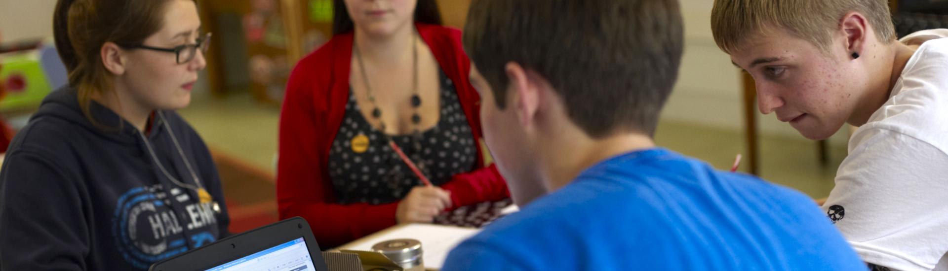 A group of pupils sitting at a table, talking and working on a laptop during a workshop