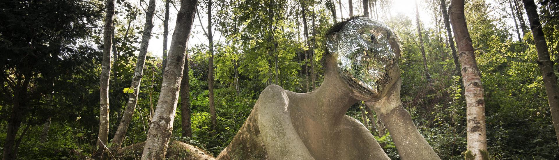 A view of a giant figure sculpture emerging from the ground with a mirrored mosaic face