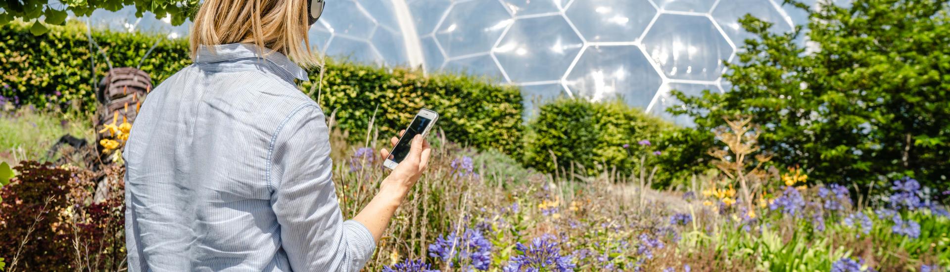 A picture of someone looking at the Eden biomes and holding their phone with their headphones on 