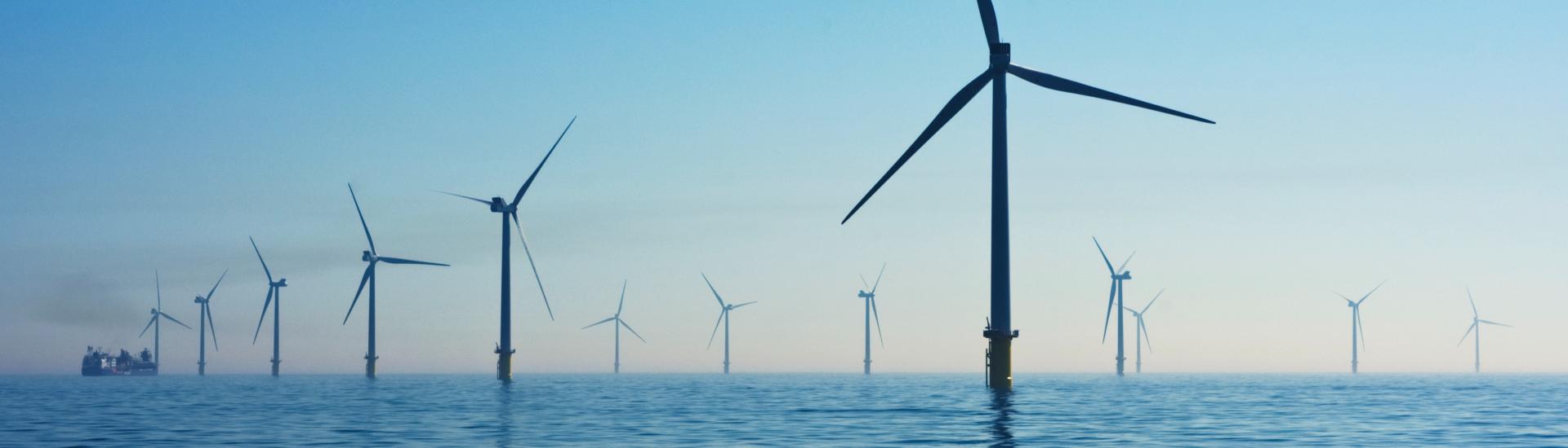 A collection of wind turbines out to sea with the sun setting in the background