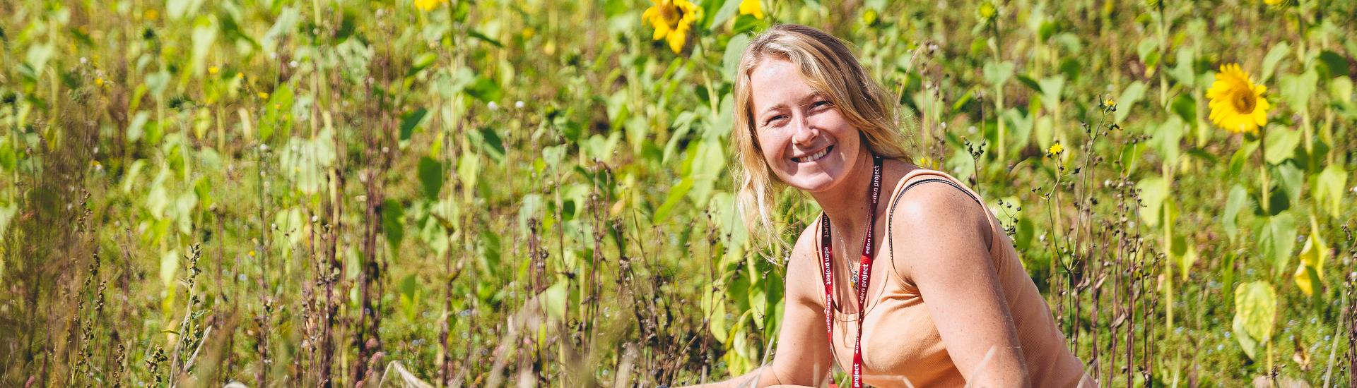 A Eden employee gardening looking to the camera surrounded by sunflowers