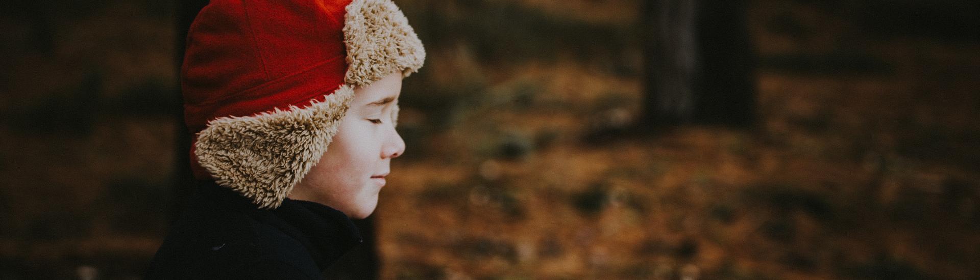 A young boy in Winter clothing stood in a woodland with his eyes closed