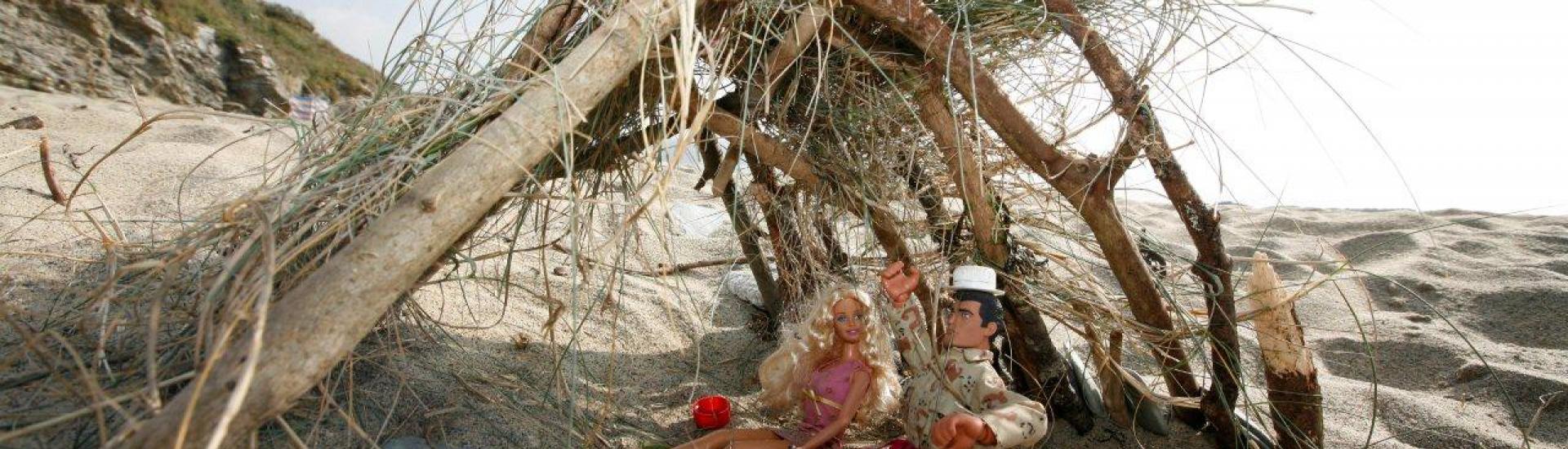 A handmade small beach hut with barbie and ken sitting under the shelter