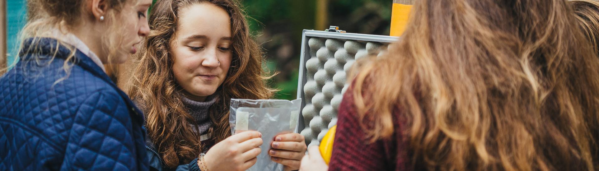 Three school pupils stood around each other looking at evidence bags 