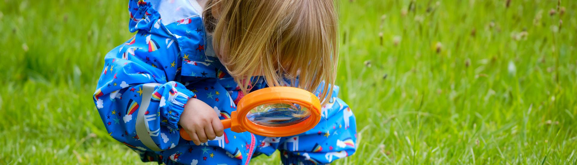 A child crouching on the ground with a magnifying glass looking for bugs