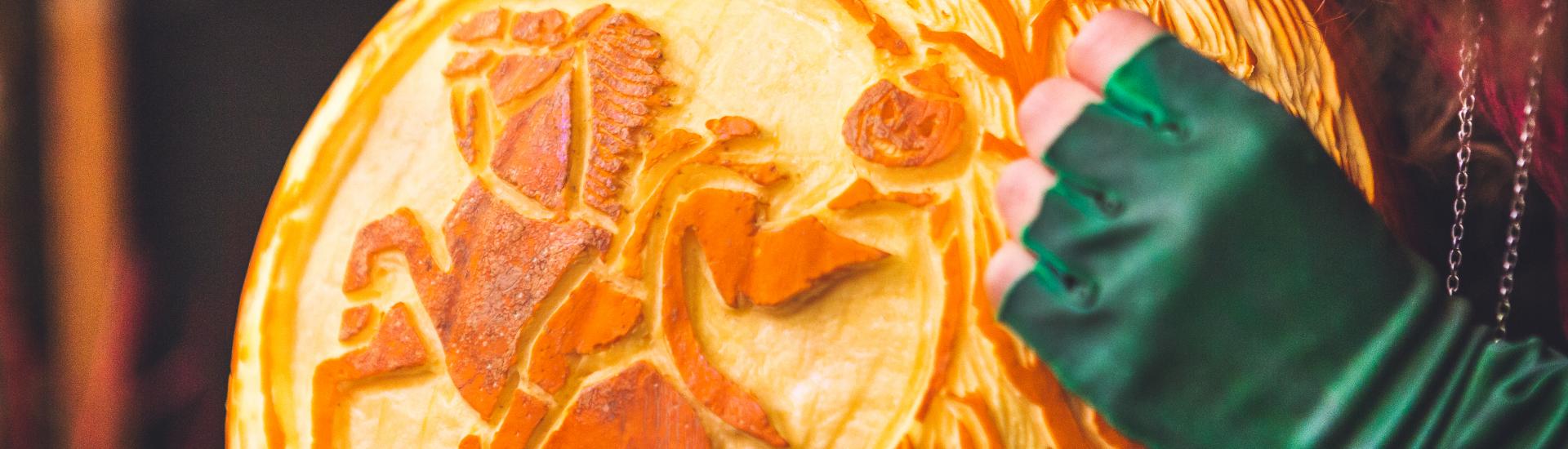 A close up of two hands carving out a design on a pumpkin