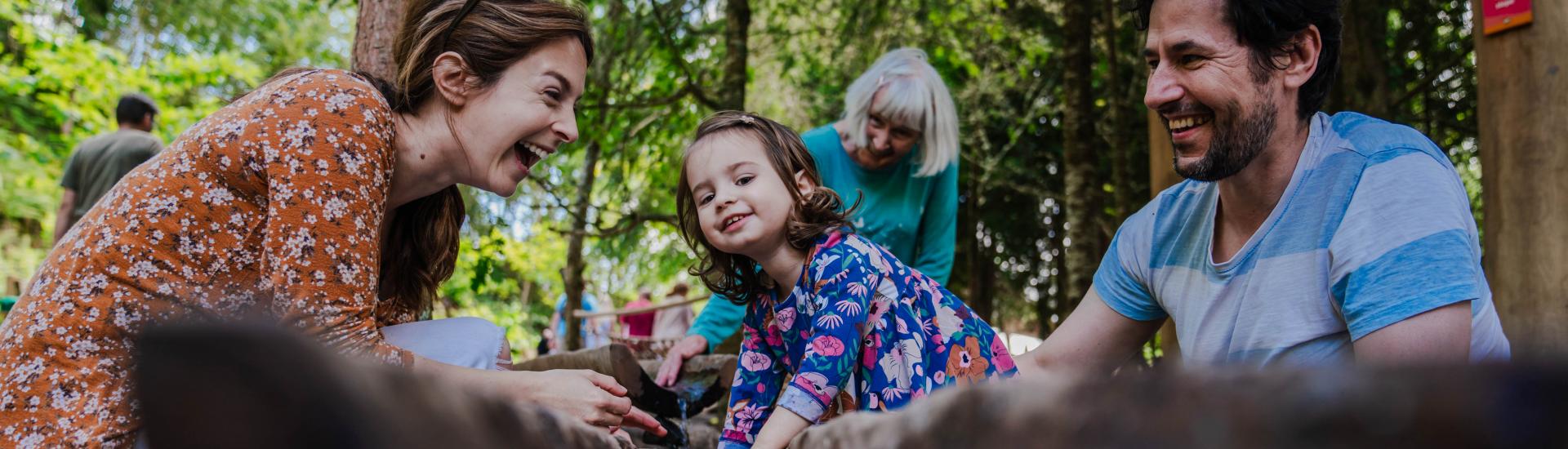 Mother, father and daughter laughing and playing in Babbling Brook, the water course part of our new adventure play area