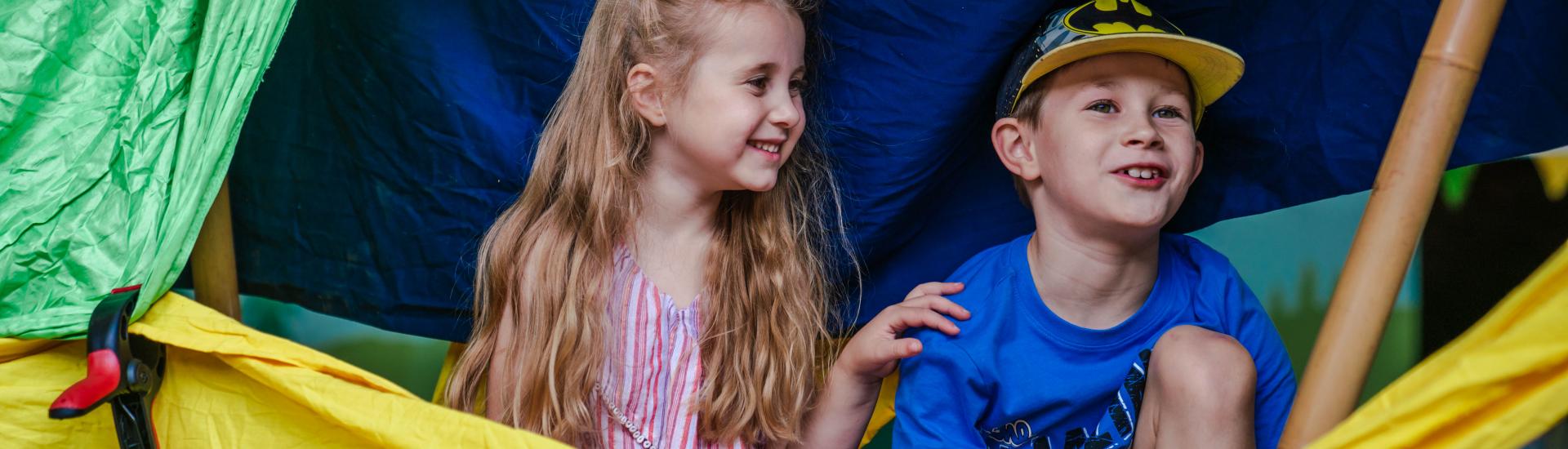 Young boy and girl smiling and hiding inside a den they created
